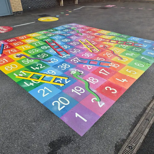 A rainbow snakes and ladders marking, numbered 1 to 100, on a school playground
